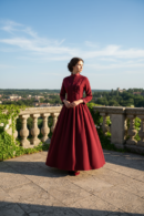 kobieta w eleganckim koku ubrana w bordową suknię balową stojąca na kamiennym balkonie