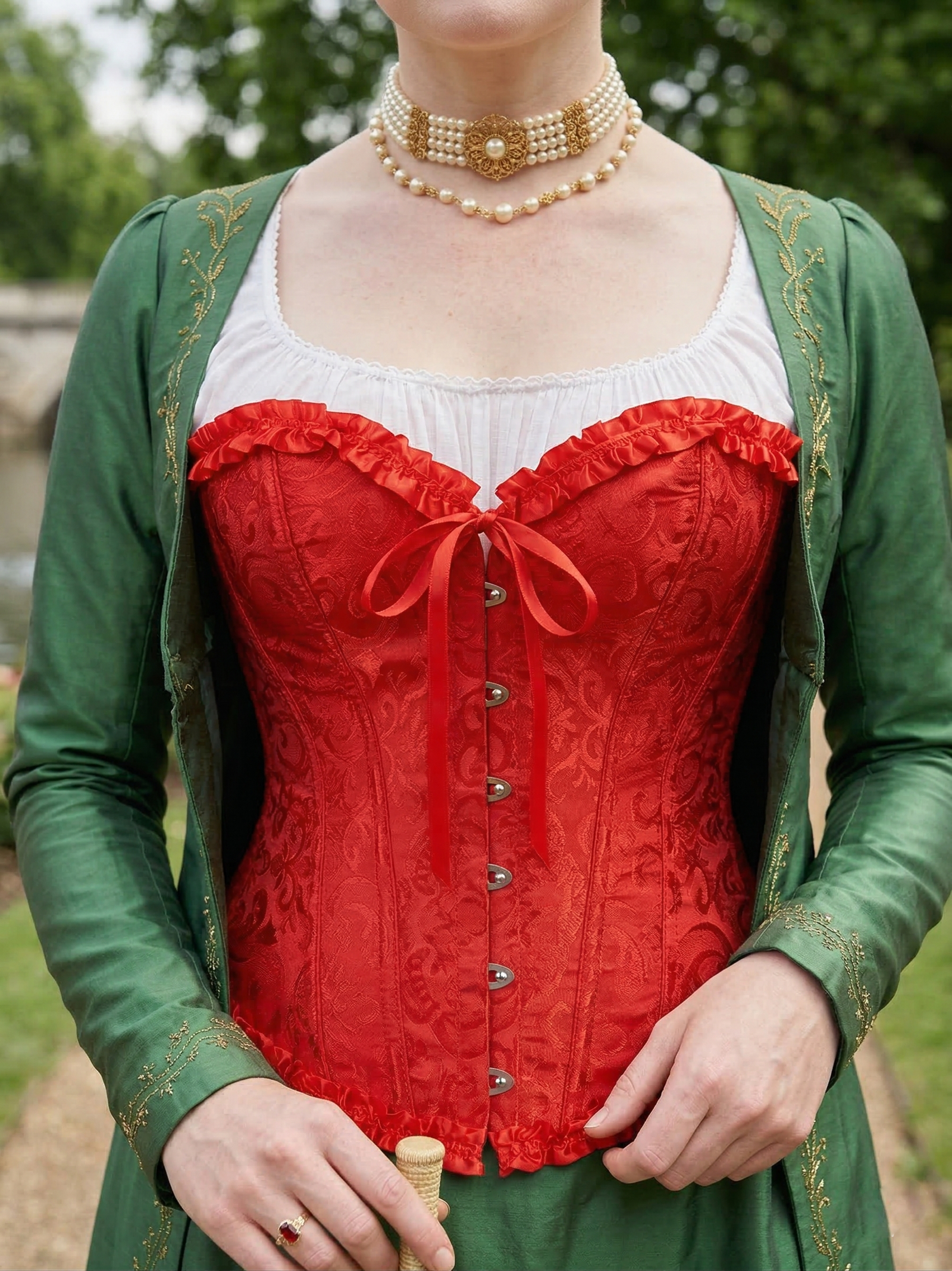 zbliżenie na czerwony gorset na kobiecie, która nosi także zieloną narzutę i perłowy naszyjnik