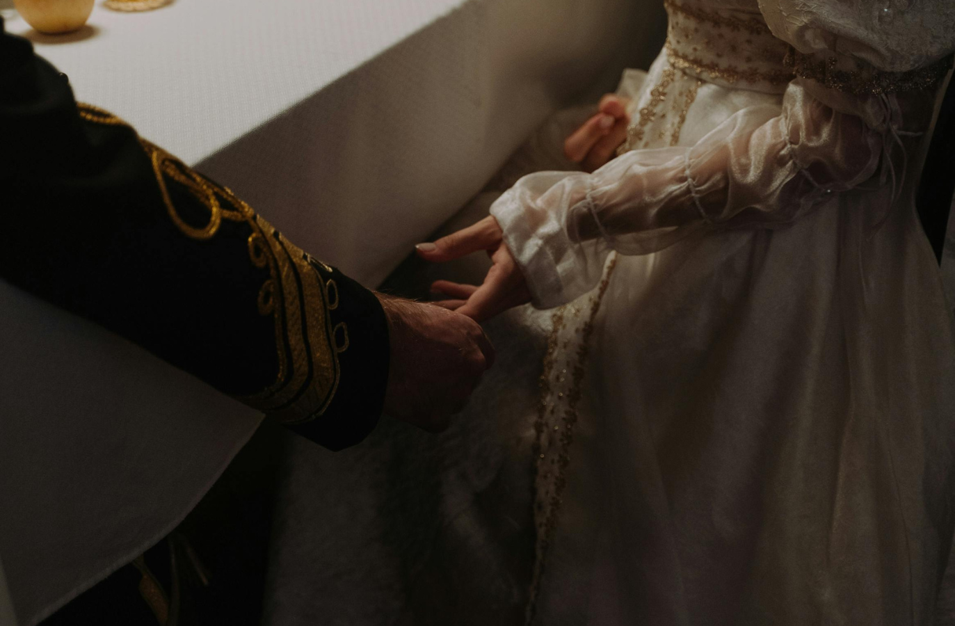 para ubrana w regencyjne kreacje trzymająca się za ręce pod stołem