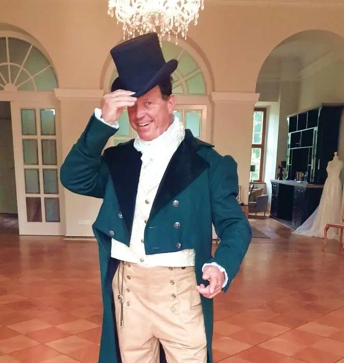 mężczyzna noszący zielony frak, białą koszulę oraz klasyczny kapelusz męski regencyjny w sali balowej