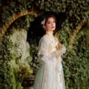 kobieta ubrana w białą elegancką suknię trzymająca czarną parasolkę koronkową w ogrodzie