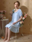 kobieta ubrana w jasnoniebieską koszulę nocną regencyjną siedząca na eleganckim krześle