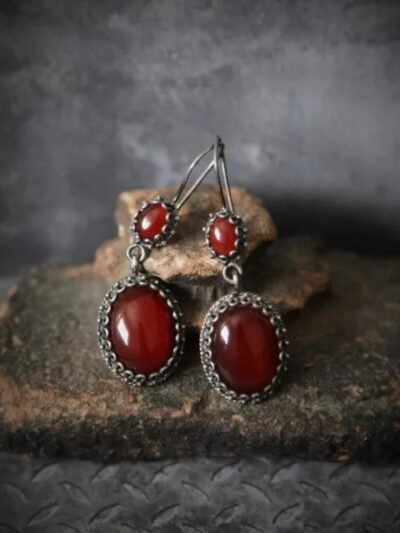 bordowe kolczyki vintage położone na brązowym kamieniu