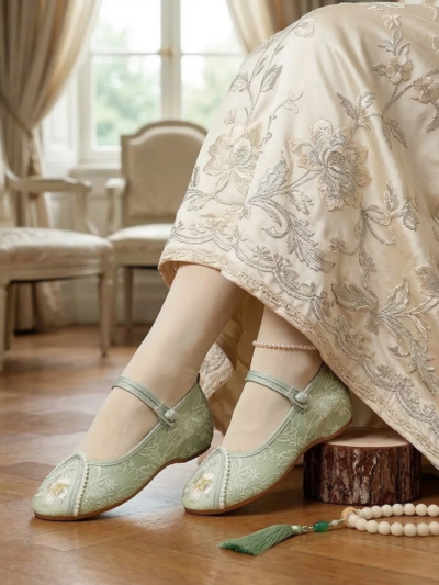 kobieta obrócona bokiem siedząca na krześle, nosząca białą suknię oraz zielone buty vintage damskie do tańca zdobione perłami