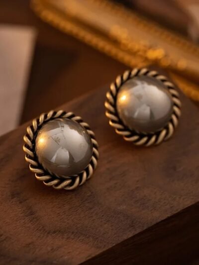 okrągłe, beżowo-szare eleganckie kolczyki vintage na drewnianym biurku