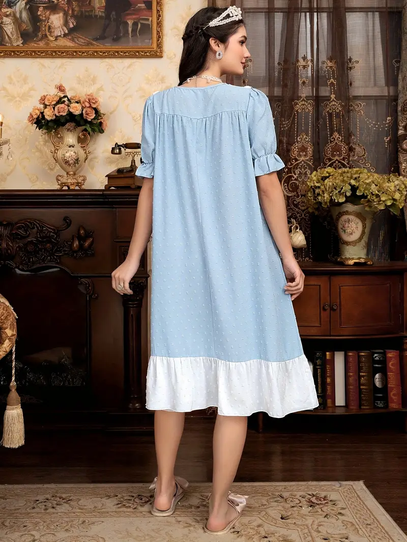 kobieta z czarnymi włosami ozdobionymi srebrną tiarą obrócona tyłem ubrana w jasnoniebieską koszulę do spania w starodawnym salonie