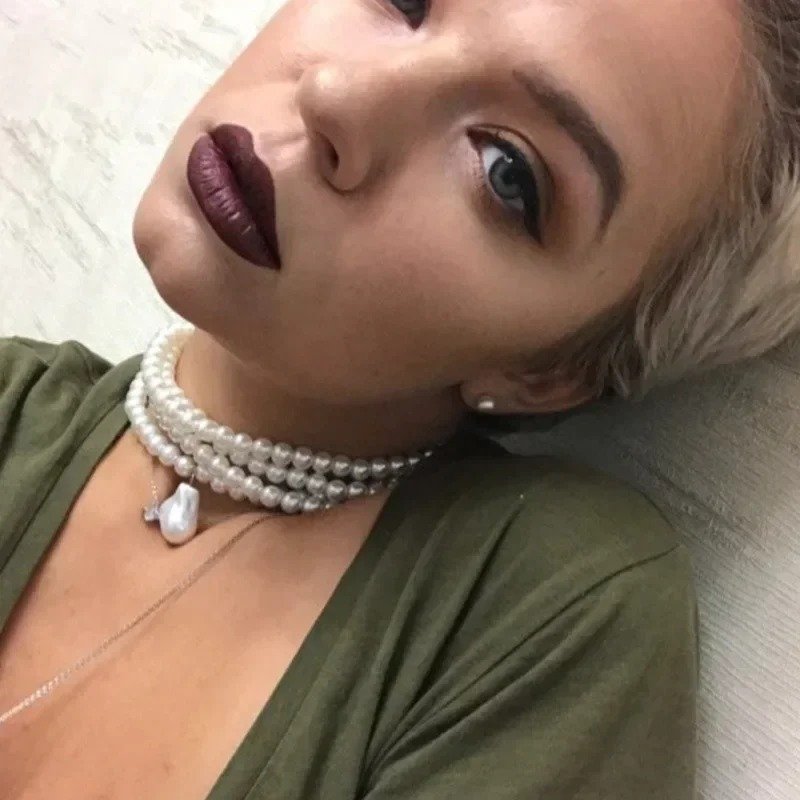 kobieta z krótkimi blond włosami oraz pomalowanymi na brązowo ustami nosząca perłowy naszyjnik vintage