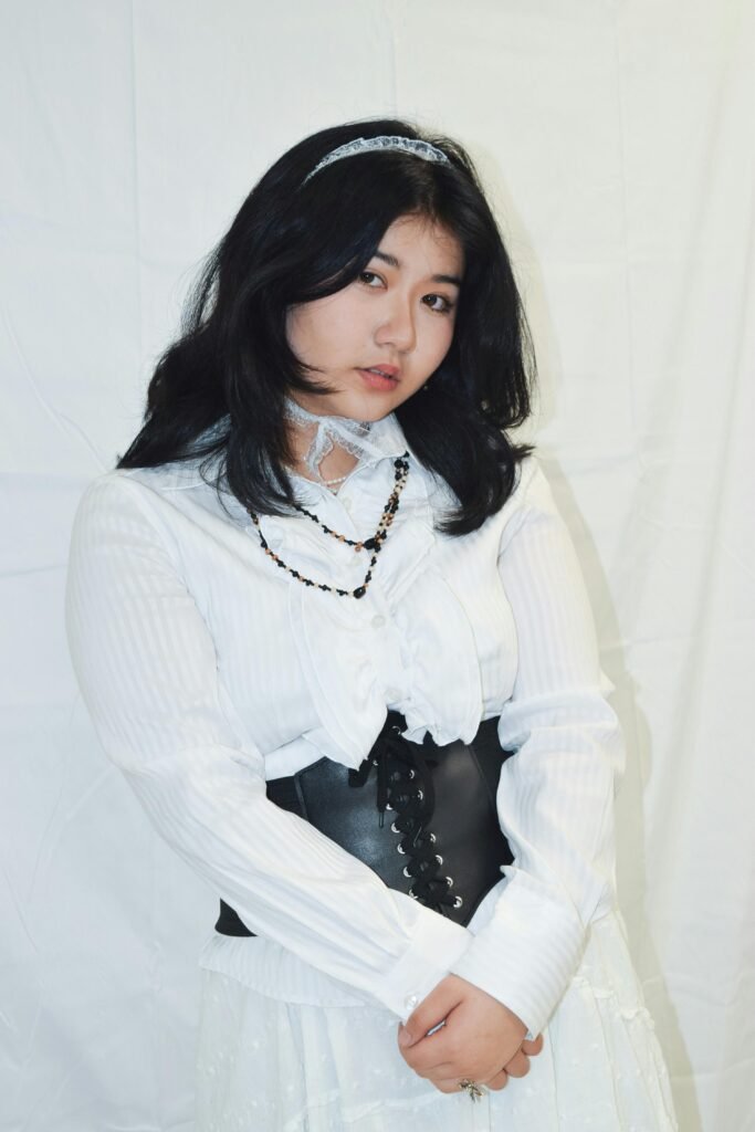 kobieta z czarnymi włosami ubrana w starodawną białą sukienkę oraz czarny pas gorsetowy