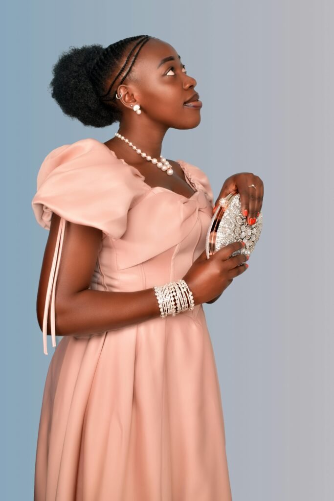 ciemnoskóra kobieta z czarnymi włosami nosząca elegancką beżową suknię balową oraz srebrną biżuterię i sebrną torebkę