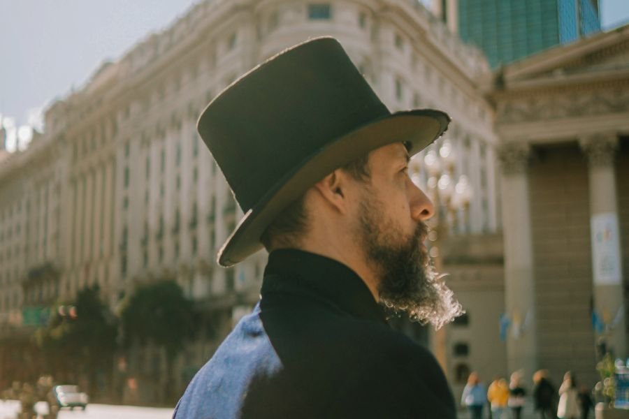 mężczyzna z brodą noszący elegancki czarny kapelusz i granatiwy płaszcz pokazując, do czego nosić kapelusz męski