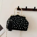 czarna torebka vintage z perłami zawieszona na ciemnym drewnianym wieszaku