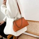 kobieta nosząca biały sweter oraz jasnobrązową torebkę w stylu vintage na ramieniu