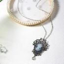 wisiorek vintage zdobiony srebrem i diamentami leżący na białym stole obok porcelanowego talerza