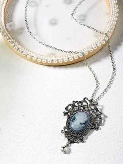 wisiorek vintage zdobiony srebrem i diamentami leżący na białym stole obok porcelanowego talerza