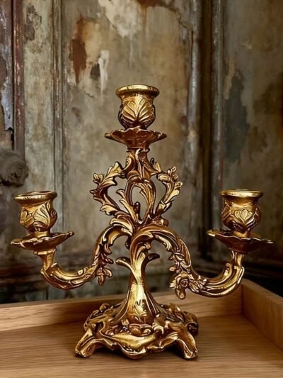 złoty barokowy świecznik położony na drewnianym stole, zielona tapeta w tle