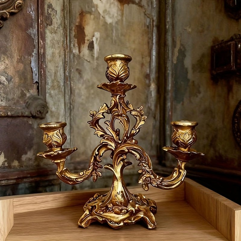 złoty barokowy świecznik położony na drewnianym stole, zielona tapeta w tle