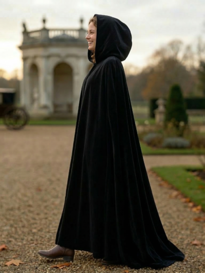 kobieta nosząca czarną pelerynę damską oraz brązowe kozaki i stojąca bokiem na ścieżce