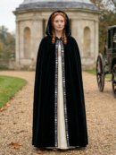 kobieta z rudymi włosami wpatrzona w dal ubrana w czarną dawną damską pelerynę na ścieżce