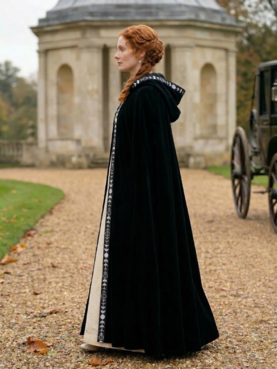 kobieta z rudymi włosami upiętymi w kok obrócona bokiem nosząca czarną dawną damską pelerynę, altana w tle