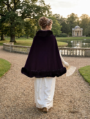 kobieta z włosami upiętymi w kok obrócona tyłem nosząca białą suknię oraz elegancką pelerynę samską, trzymająca wachlarz