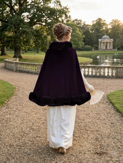 kobieta z włosami upiętymi w kok obrócona tyłem nosząca białą suknię oraz elegancką pelerynę samską, trzymająca wachlarz