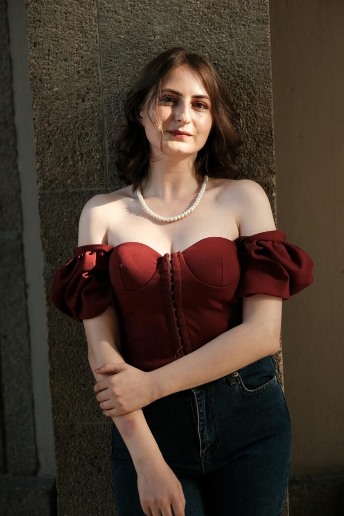 kobieta z krótkimi brązowymi włosami nosząca czerowny gorset oraz jeansy