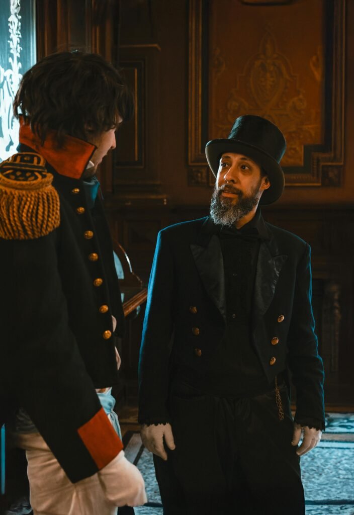 hrabia ubrany w czarny melonik, czarny frak oraz elegancki płaszcz rozmawiający z księciem w szykownym mundurze