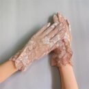 kobieta nosząca jasnoróżowe rękawiczki balowe oraz krzyżująca ręce na szarym tle