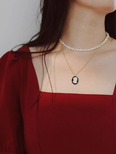 kobieta z ciemnobrązowymi włosami nosząca bordową sukienkę oraz czarny owalny naszyjnik vintage