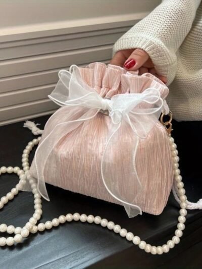 jasnoróżowa płócienna torebka vintage zdobiona białą kokardą i perłami na czarnym biurku