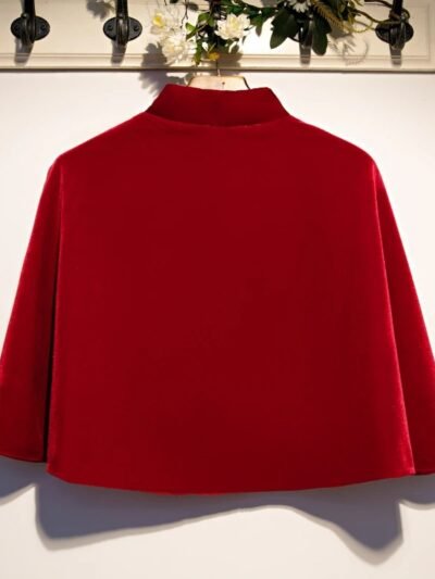 czerwona aksamitna peleryna damska obrócona tyłem zawieszona na wieszaku na białej ścianie