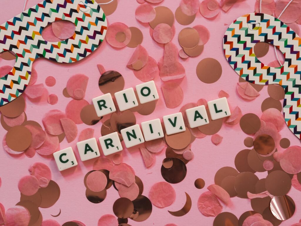 scrabble ułożoe w literki "RIO CARNIVAL" na rózowym tle z cekinami jako symbol tego, jaka sukienka na bal karnawałowy