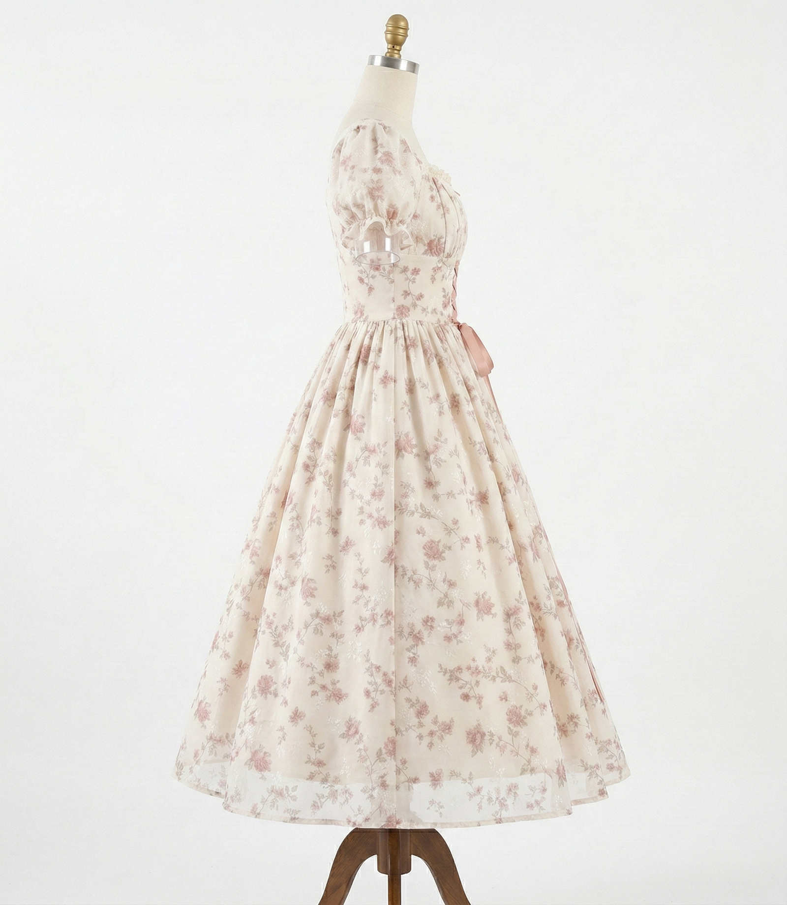 Kobieta w kremowej sukience midi w różowe kwiaty, stojąca w ogrodzie pełnym róż