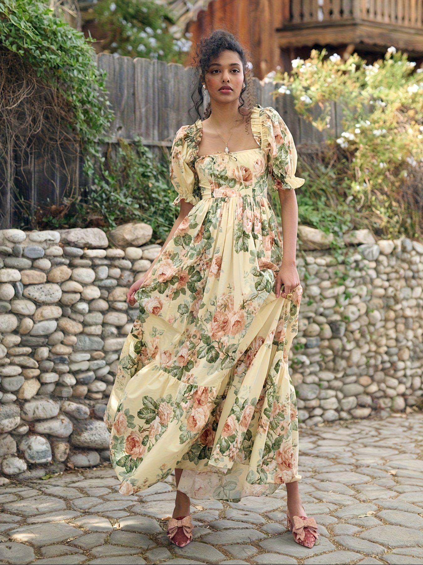 kobieta z brązowymi włosami upiętymi kok stojąca z pewnością siebie w żółtej sukni balowej midi na kamieniach