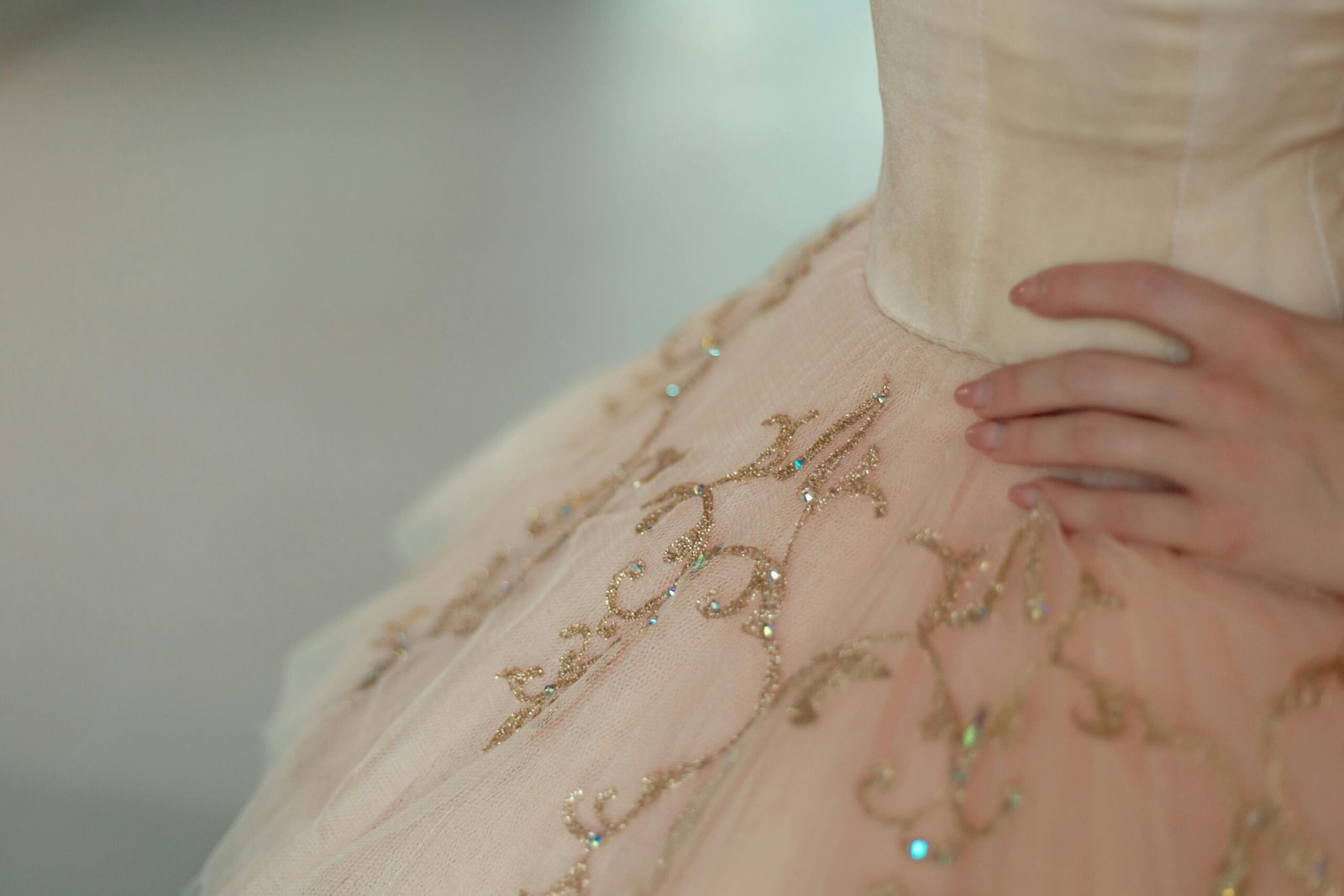 dłoń kobiety na beżowym tiulowym materiale sukienki ozdabianym złotem jako symbol tego, gdzie kupić sukienkę na bal